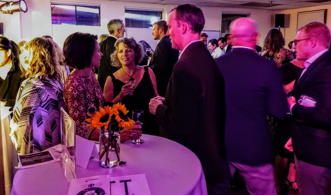 A candid photo of a small group of people standing around a table talking while at a formal affair.