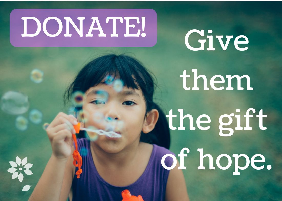 child with dark hair blowing bubbles in a grassy field, give them the gift of hope, donate here